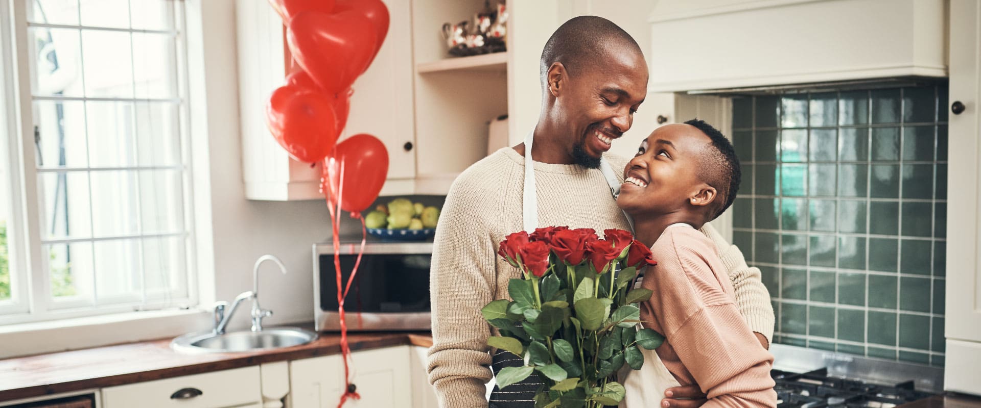 LCV-Valentines-Day-2026 Couple smiling and holding red roses in a kitchen decorated with heart balloons celebrating Valentine’s Day from Lake Crest Village